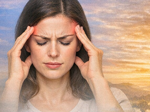 Frau mit Kopfschmerz, die sich die Schläfen hält. Im Hintergrund Sonnenuntergang.