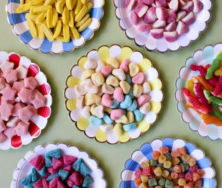 Bunte Süßigkeiten auf weißen Tellern, angeordnet in verschiedenen Formen und Farben.